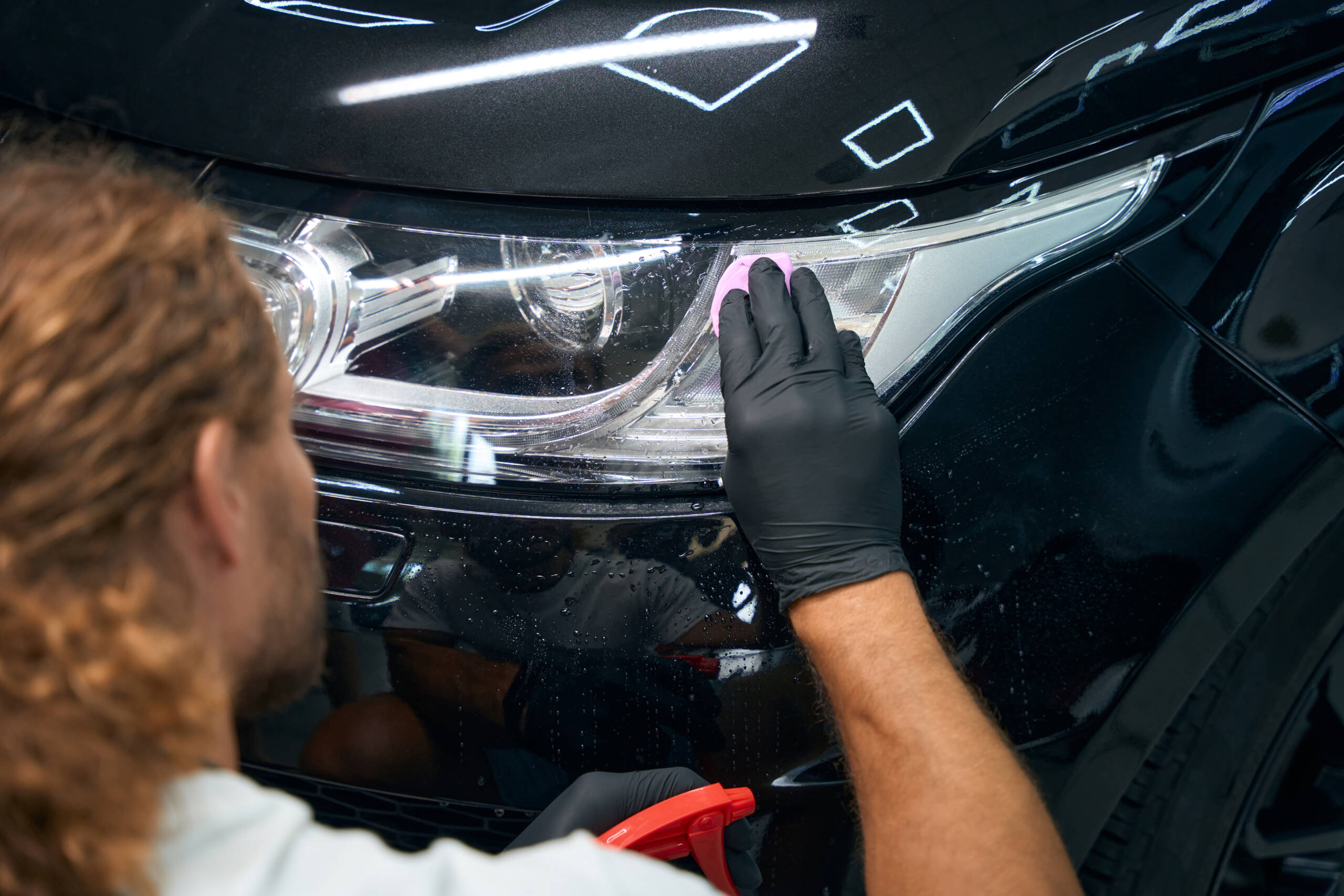 Male is working in a car workshop detailing black car Male is working in a car workshop detailing a black car, he is using protective gloves